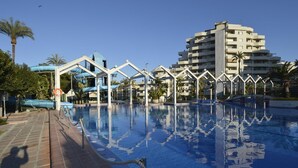 A swimming pool with a clear blue water surface, surrounded by a brick walkway and palm trees.