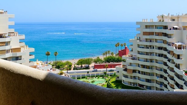 A coastal hotel with multiple balconies, a beach view, and a clear blue sky.