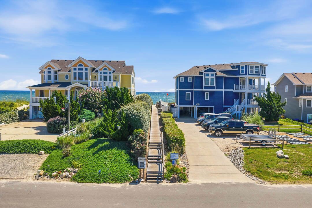 A coastal residential area with multi-story houses, a paved driveway, and a parking area.