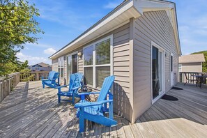A wooden deck with blue Adirondack chairs and a small table.