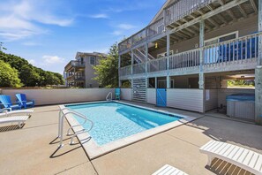 A swimming pool with a wooden deck, lounge chairs, and a multi-level building with balconies.