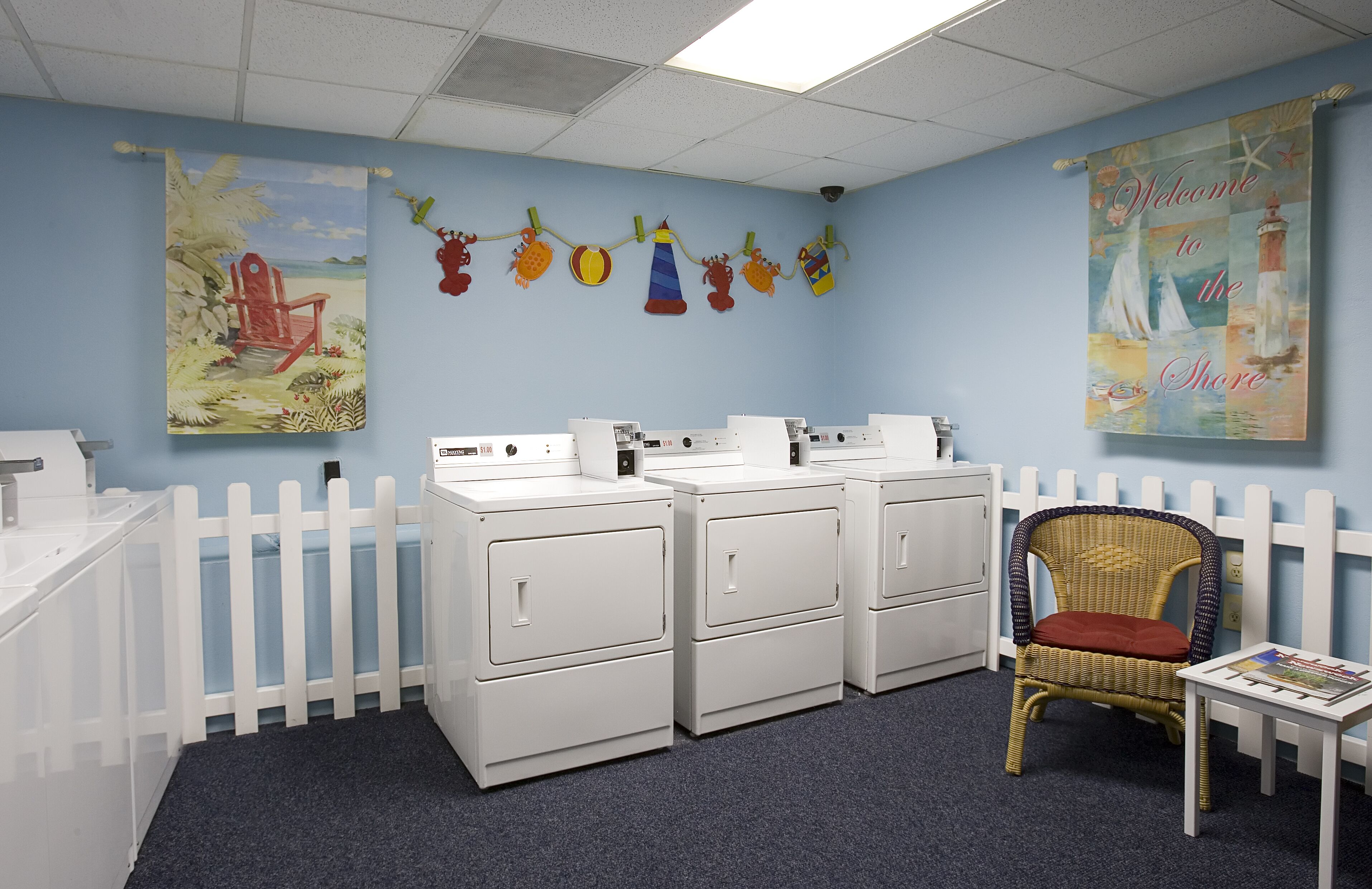 A laundry room with white cabinets, a wicker chair, and a wall with nautical-themed decorations.