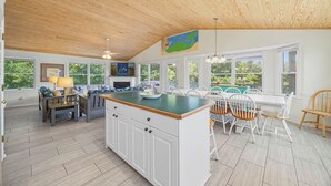 Une cuisine spacieuse avec un plafond en bois, de grandes fenêtres et un coin repas comprenant des chaises blanches et une table.