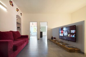 A modern living room with a red sofa, a flat-screen TV mounted on the wall, and a wooden side table with books.