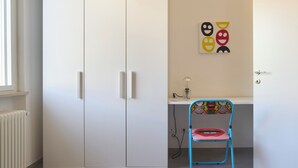 Una habitación con un armario blanco, un escritorio con una silla y una pared decorada con un dibujo de una cara sonriente.