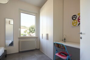 Un dormitorio infantil con cama, ventana, radiador, escritorio y silla.