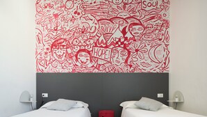Una habitación de hotel con dos camas, un cesto de basura rojo y un mural en la pared con motivos rojos y blancos.