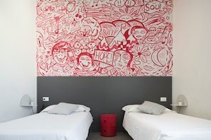Una habitación de hotel con dos camas, un cesto de basura rojo y un mural en la pared con motivos rojos y blancos.