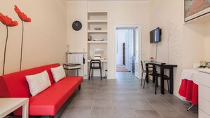 Un salon moderne avec un canapé rouge, un coin repas avec une table et des chaises, un espace cuisine et un couloir menant à une autre pièce.
