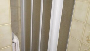 Une salle de bain avec un espace douche fermé, des murs carrelés et une serviette accrochée au mur.