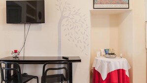 Une chambre d’hôtel équipée d’un téléviseur à écran plat fixé au mur, d’une table avec deux chaises, d’une petite table recouverte d’une nappe blanche et rouge, et d’un tableau encadré représentant le Musée des Beaux-Arts de Boston.
