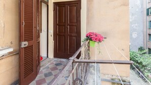 Un balcon avec un sol à carreaux, une porte marron et un pot de fleurs contenant des fleurs roses.