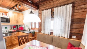 Una cocina acogedora de estilo rústico con armarios de madera, una mesa de comedor con un mantel individual y una ventana con cortinas.