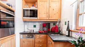 Una cocina compacta con armarios de madera, microondas, lavavajillas y un pequeño comedor con mantel a rayas.