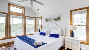 Una camera da letto con un letto grande, pavimento in legno, una ventola a soffitto e diverse finestre.