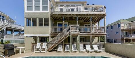 A two-story building with a pool, outdoor seating, and a wooden deck.
