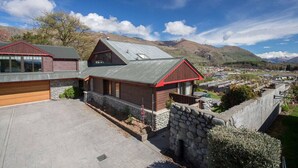 A two-story house with a stone foundation and a metal roof, surrounded by a stone wall and a small garden. - Bullock Creek Chalet · Lake & mountain views (Wanaka)