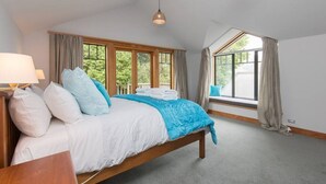 A bedroom with a large bed, a nightstand, a window with curtains, and a view of greenery outside. - Bullock Creek Chalet · Lake & mountain views (Wanaka)