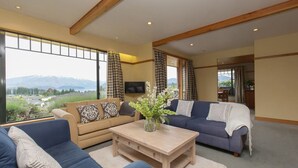 A spacious living room with a large window offering a mountain view, two sofas, a coffee table, and a television mounted on the wall. - Bullock Creek Chalet · Lake & mountain views (Wanaka)