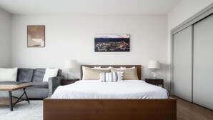 Ein modernes Schlafzimmer mit einem großen Bett, einer Couch, einem Nachttisch und einem Stadtbild an der Wand.