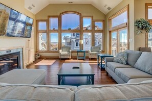 Un salón amplio con chimenea, asientos cómodos y ventanas grandes con vista al océano.