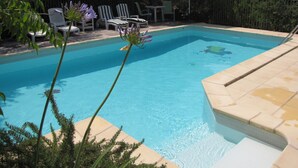 Une piscine à l’eau d’un bleu limpide, entourée de chaises longues et d’une clôture.