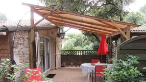 Une terrasse extérieure avec un mur en pierre, une pergola en bois et une table entourée de chaises rouges.