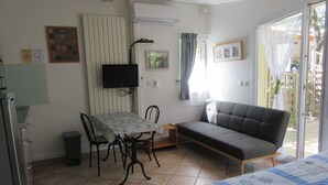Une pièce comprenant une table à manger, des chaises, un canapé, un téléviseur et une fenêtre avec des rideaux.