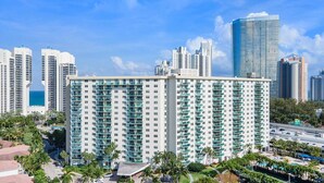 A high-rise hotel with multiple balconies, surrounded by palm trees and a clear blue sky. - Family-Friends Getaway- Pool, Beach & Parking free (Sunny Isles Beach)