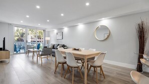 A modern living room with a dining area, large windows, and a view of palm trees. - Family-Friends Getaway- Pool, Beach & Parking free (Sunny Isles Beach)
