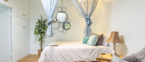 A bedroom with a bed, bedside table, lamp, and a potted plant.