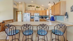 Una cocina con armarios de madera, una isla central con taburetes de bar, un refrigerador, microondas y estufa.