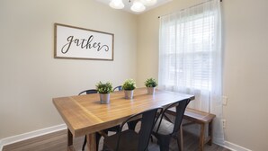 A dining area with a wooden table, four chairs, and three potted plants.