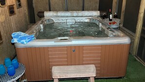 A hot tub with a wooden bench in front, surrounded by wooden walls and string lights.
