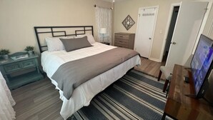 A bedroom with a bed, bedside table, lamp, and a TV.