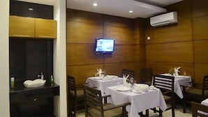 A restaurant with wooden panel walls, a TV mounted on the wall, and tables set with white tablecloths and centerpieces. - Green Paradise Hotel (Yangon)
