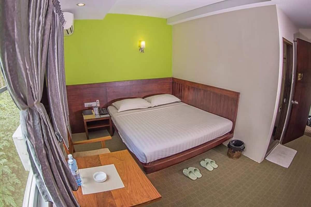 Una habitación de hotel con cama, mesita de noche, lámpara y vistas al exterior.