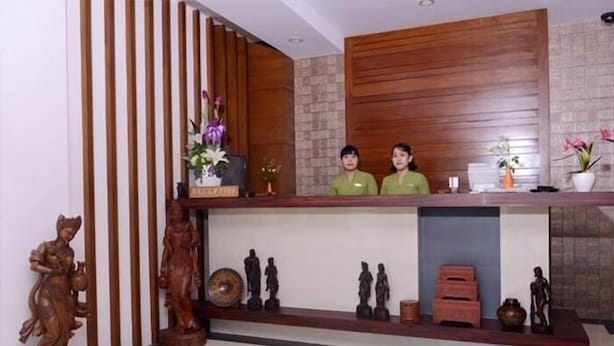 A reception desk with two staff members, wooden paneling, and various decorative items including statues and pottery. - Green Paradise Hotel (Yangon)