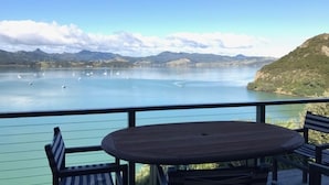 A terrace with a table and chairs overlooking a calm lake with boats and mountains in the background. - Gorgeous Waterfront Views and Private Access to Bay (Wyuna Bay)