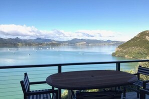 Eine Terrasse mit Tisch und Stühlen mit Blick auf einen ruhigen See, im Hintergrund Boote und Berge.