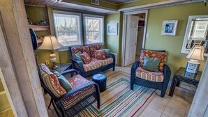 Una sala de estar acogedora con muebles de mimbre, un tapete a rayas y una puerta que da a otra habitación.