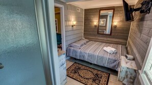 Un dormitorio con una cama, una mesita de noche, un espejo y un televisor montado en la pared.