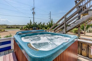 Un jacuzzi en una terraza de madera con vista a una carretera y colinas al fondo.