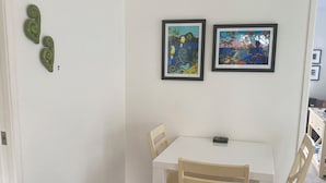 A dining area with a white table and wooden chairs, two framed artworks on the wall, and a door with a decorative green object.