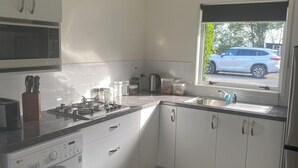 A modern kitchen with white cabinets, a built-in washing machine, a gas stove, and a window with a view of a car outside.