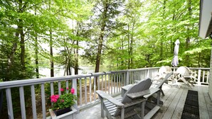 A wooden deck with a white railing, a table with chairs, and a potted plant with pink flowers. - Beautiful Waterfront Home w/ Canoe & 1 Person Kayak. Close to North Conway (Madison)