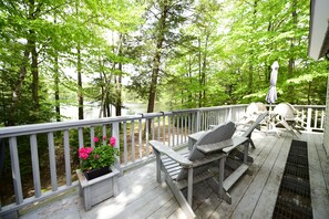 Une terrasse en bois avec une balustrade blanche, une table avec des chaises et un pot de fleurs contenant des fleurs roses.