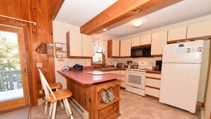 A kitchen with wooden cabinets, a refrigerator, a microwave, and a sink. There is a wooden island with a bench and a decorative heart-shaped shelf. - Beautiful Waterfront Home w/ Canoe & 1 Person Kayak. Close to North Conway (Madison)