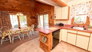 A wooden cabin interior with a dining area, kitchen, and a large window with curtains. - Beautiful Waterfront Home w/ Canoe & 1 Person Kayak. Close to North Conway (Madison)