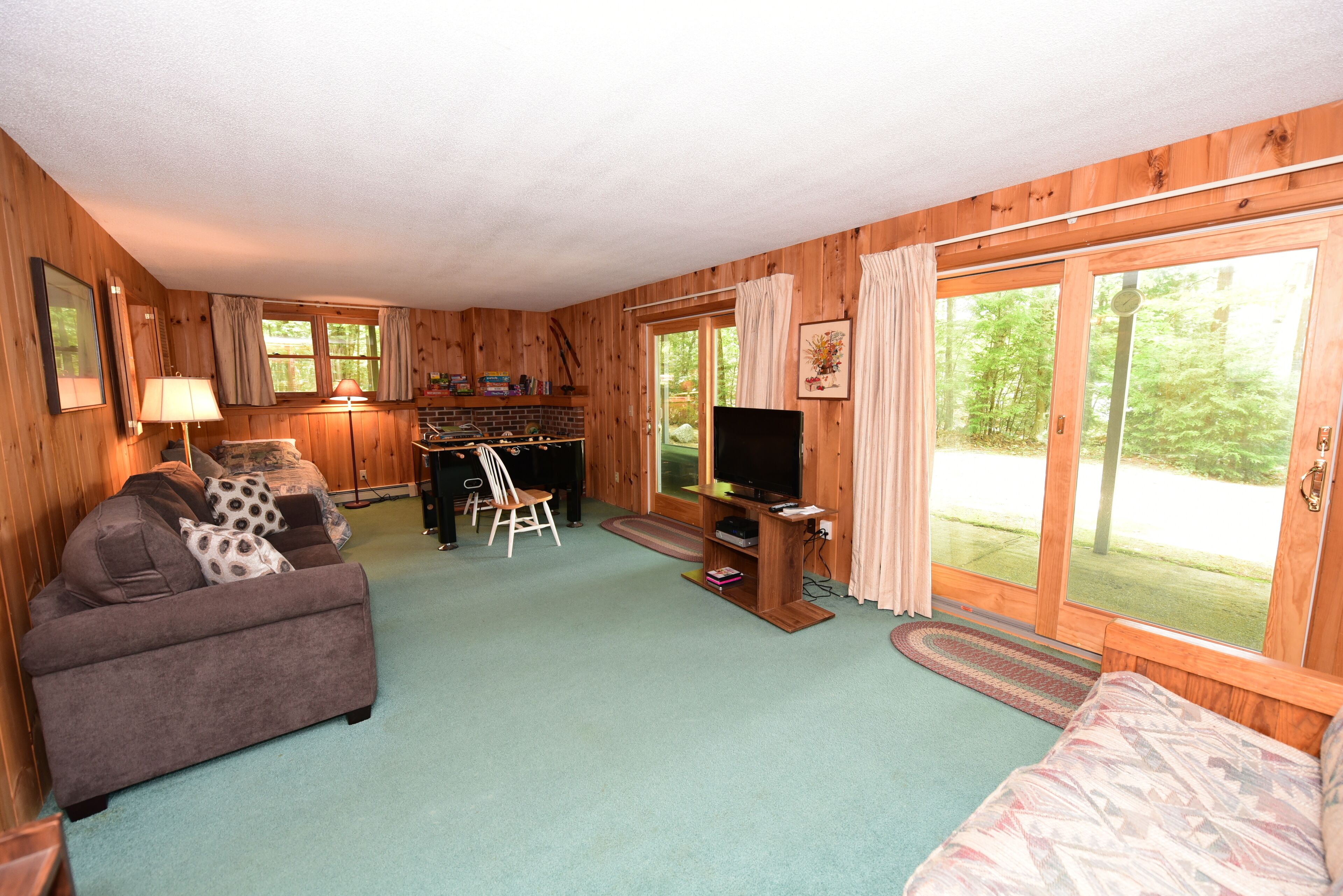 A cozy cabin interior with a sofa, a television, a dining area, and large windows offering a view of the outdoors.